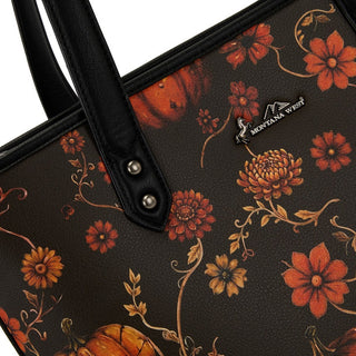 Close-up of a black tote bag with orange pumpkins and fall floral design, black handles, and Montana West logo.