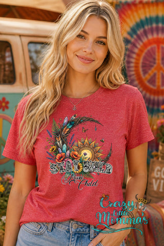 A woman smiles, wearing a red "Stay Wild Moon Child" tee with a floral crescent moon and sunflower graphic.