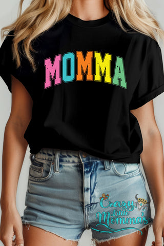 A woman wears a black Neon Momma Tee with "MOMMA" in distressed neon pink, blue, orange, and green letters.