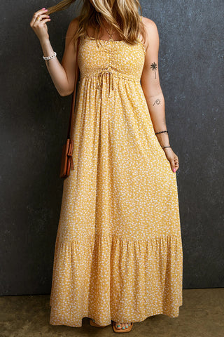 A woman wears a yellow floral maxi dress with a smocked bodice, tie detail, and tiered skirt.