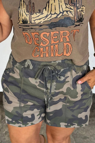 A person wearing Desert Trail Camo Shorts with a drawstring waist and a "Desert Child" t-shirt.