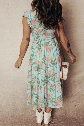 Back view of a woman wearing a light blue floral prairie midi dress with smocked bodice and ruffled sleeves.