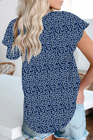 Back view of a woman wearing a navy floral flutter top with a rounded hem and light wash denim shorts.