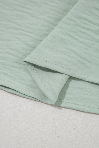 Close-up of the light green Prairie Ruffle Blouse fabric, showing its textured weave and stitched hem.