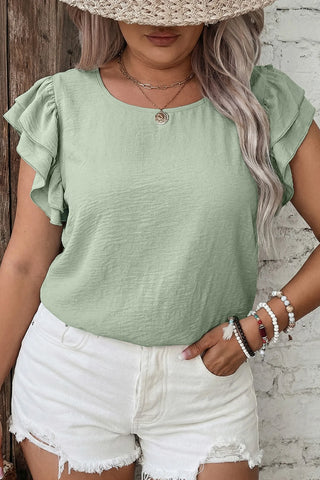 Woman wearing a light green Prairie Ruffle Blouse with ruffled sleeves, paired with white shorts.