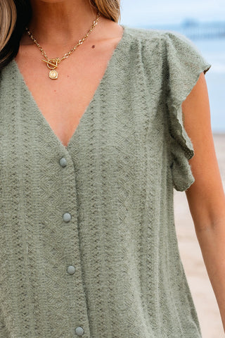 Close-up of a woman wearing a sage ruffle button top with a V-neck and a gold necklace.