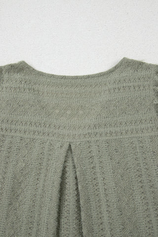 Close-up of the back of a sage ruffle button top, showing textured fabric and a central pleat.