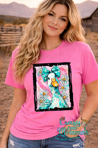A woman in a pink tee with a graphic of a duck wearing a blue bow, surrounded by daisies.