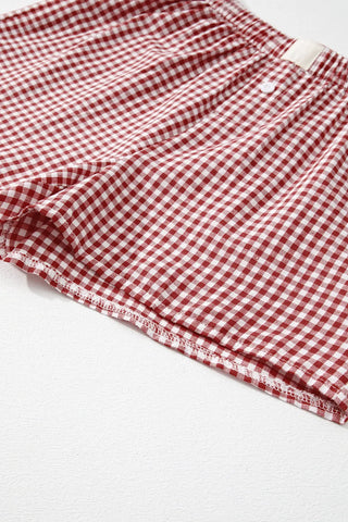 Close-up of red and white gingham shorts with a white button and elastic waistband, on a white background.