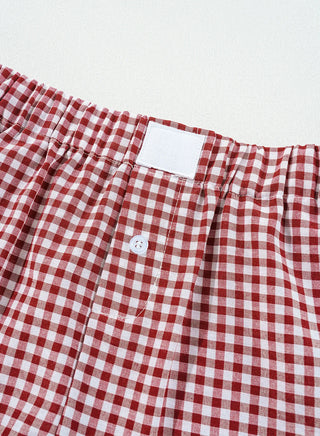 Close-up of red and white gingham shorts with an elastic waistband, a white tag, and a single white button.