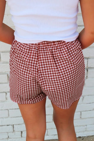 Back view of a person wearing red and white gingham shorts with an elastic waistband and a white top.