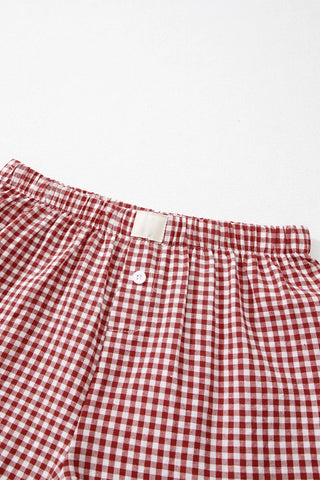 Close-up of red and white gingham shorts with an elastic waistband, a white button, and a small white label.