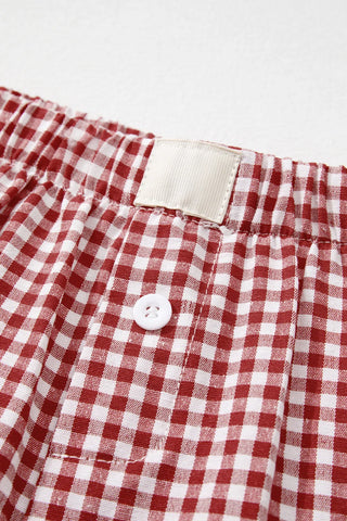 Close-up of red and white gingham shorts with an elastic waistband, a white button, and a blank white label.