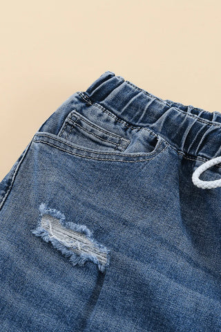 Close-up of blue Western distressed jeans with an elastic waistband, drawstring, and a ripped detail on the thigh.