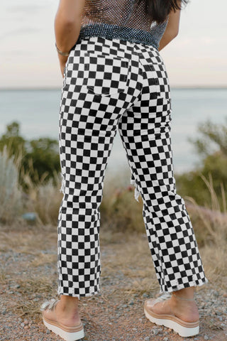 Rear view of a person wearing black and white checkerboard distressed jeans with a frayed hem.