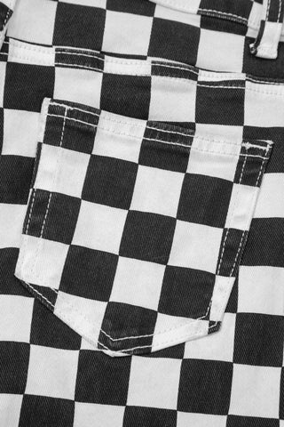 Close-up of the back pocket of black and white checkerboard distressed jeans with white stitching.