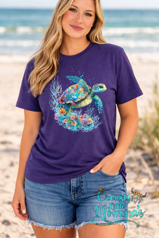 Woman in a purple tee with a colorful watercolor sea turtle surrounded by coral and flowers.