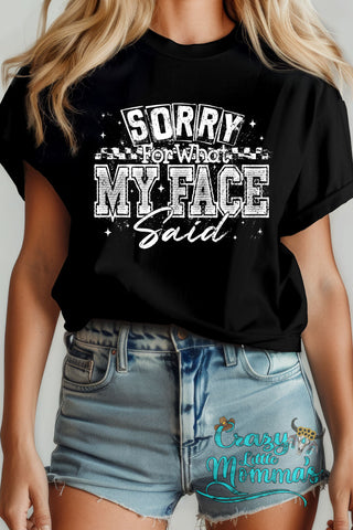 A woman wears a black "Sorry For What My Face Said" tee with white distressed text.