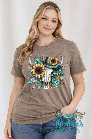 A woman models a brown Sunflower Cow Skull Tee with a cow skull, sunflowers, and turquoise feathers.