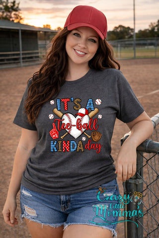 Woman in a red cap and distressed denim shorts wearing a graphite tee with "It's a Tee-ball Kinda Day" graphic.