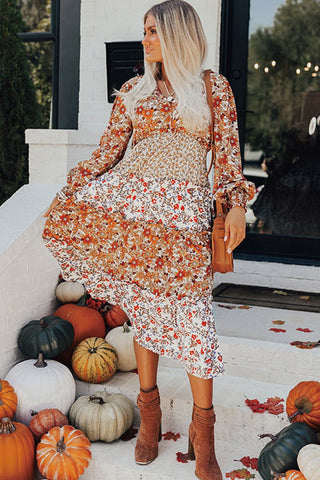 Woman in a floral dress standing in front of pumpkins on a staircase.