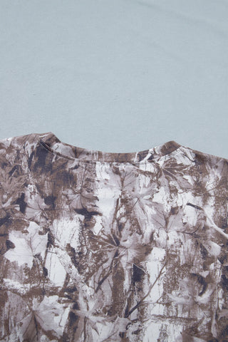 Close-up of an earthy camo crewneck tee with a brown, white, and gray leaf and branch pattern.