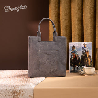 Gray Wrangler tote bag with an embroidered Aztec design on the front pocket, next to a western magazine.
