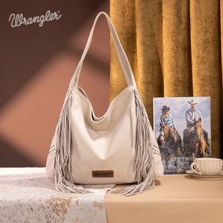 Beige Wrangler hobo bag with studded details and long fringe on both sides, displayed on a western-themed surface.