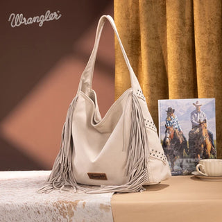 Beige Wrangler hobo bag with fringe and stud details, displayed on a cowhide rug.