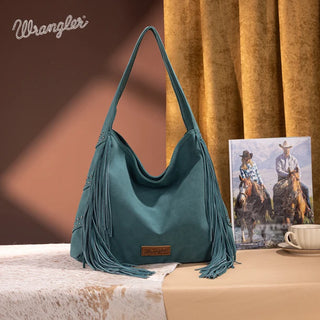 Turquoise Wrangler hobo bag with studded details and long fringe, displayed on a table with a western-themed book.