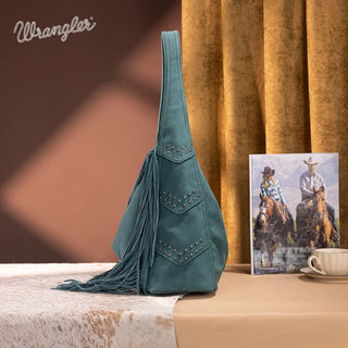 Turquoise Wrangler hobo bag with studded chevron details and long fringe, sitting on a cowhide rug.