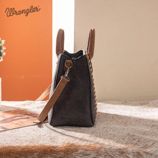 Side view of a dark gray Wrangler Whipstitch Crossbody Bag with brown handles and strap, on a fur rug.