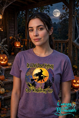 Woman wearing a heather purple Dark Highway Witch Tee with a witch flying on a broomstick against a full moon.